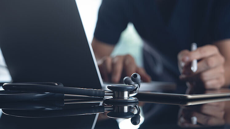 Arzt bei der Arbeit an einem Laptop und einem digitalen Tablet in einer Arztpraxis | Foto: ©tippapatt – stock.adobe.com
